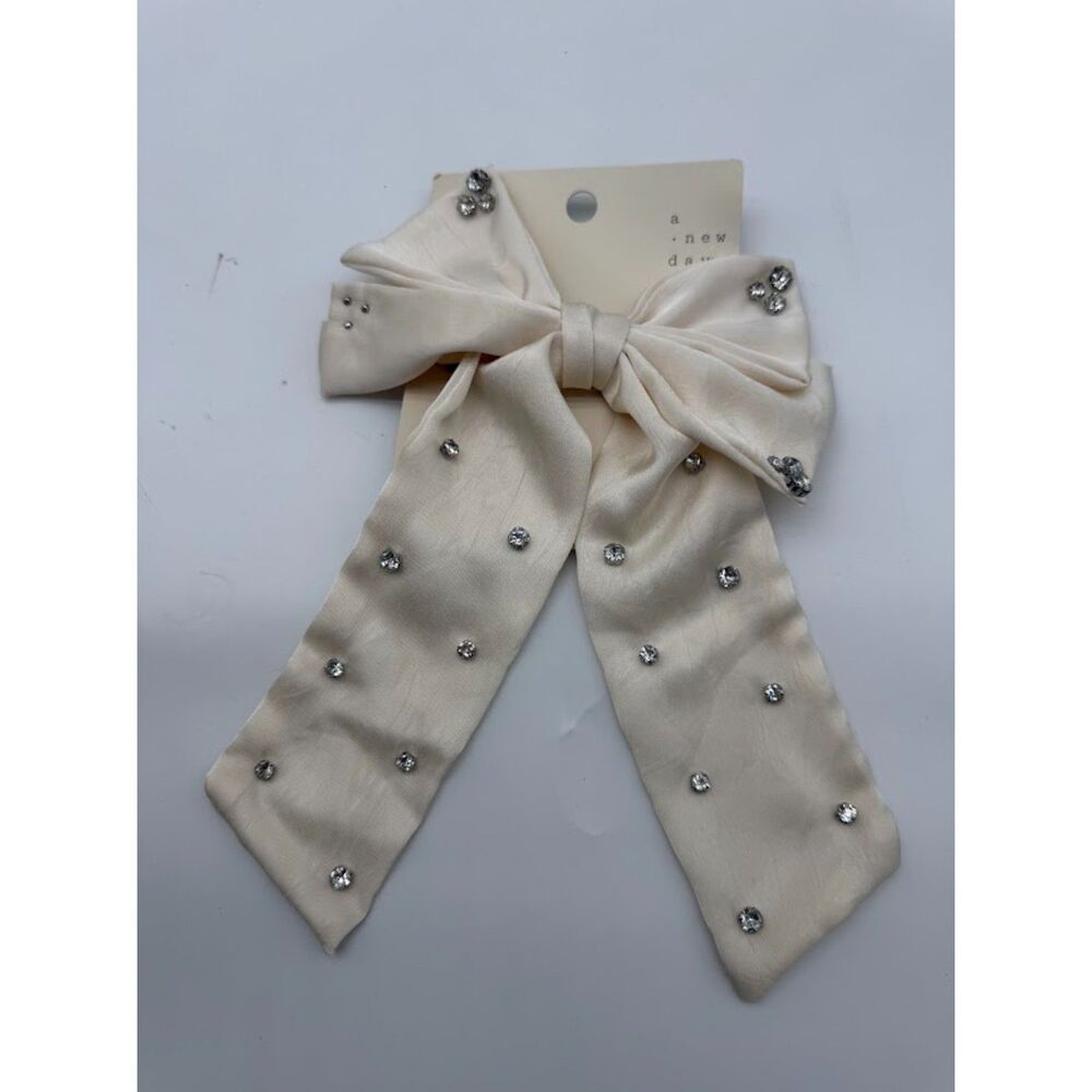 cream-colored satin bow hair clip features rhinestone embellishments.